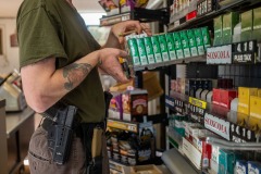 Charles Bobo wears a Glock, three magazines and a knife on a tactical belt while he works the register at the gas station in the village. With no local law enforcement, residents feel a responsibility to protect their property, family, and the rest of the community.